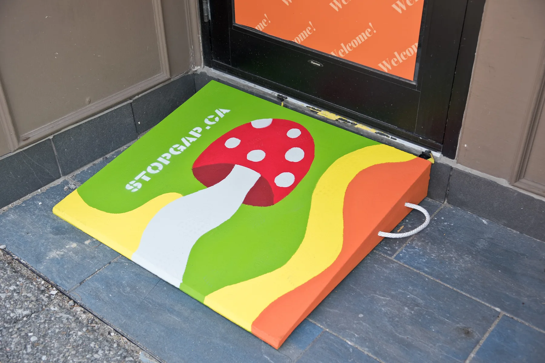 The painted mushroom accessibility ramp, a red-and-white mushroom on green, yellow and orange waves, at the door of Roots Community Services in downtown Brampton