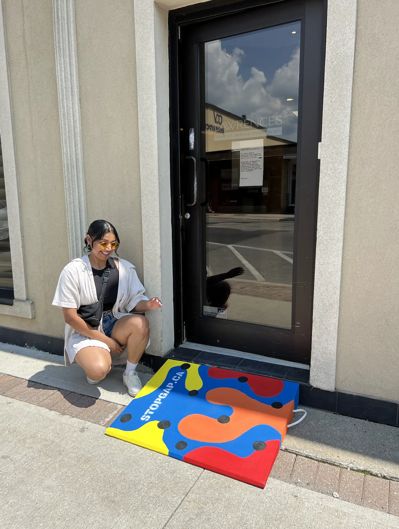 Saphera crouching beside a painted ramp in red, blue, orange and yellow at a storefront doorway in downtown Brampton