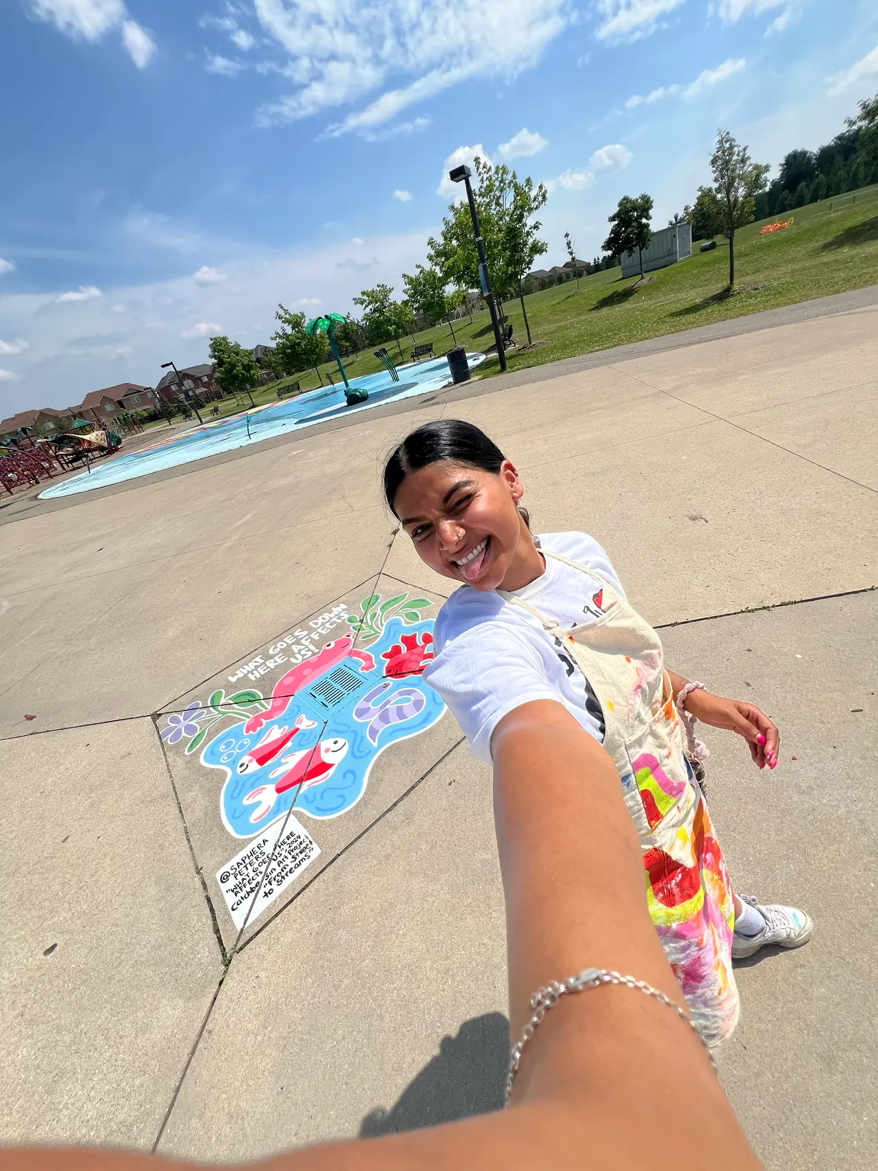Saphera crouching beside the finished underwater catch basin mural by a splash pad