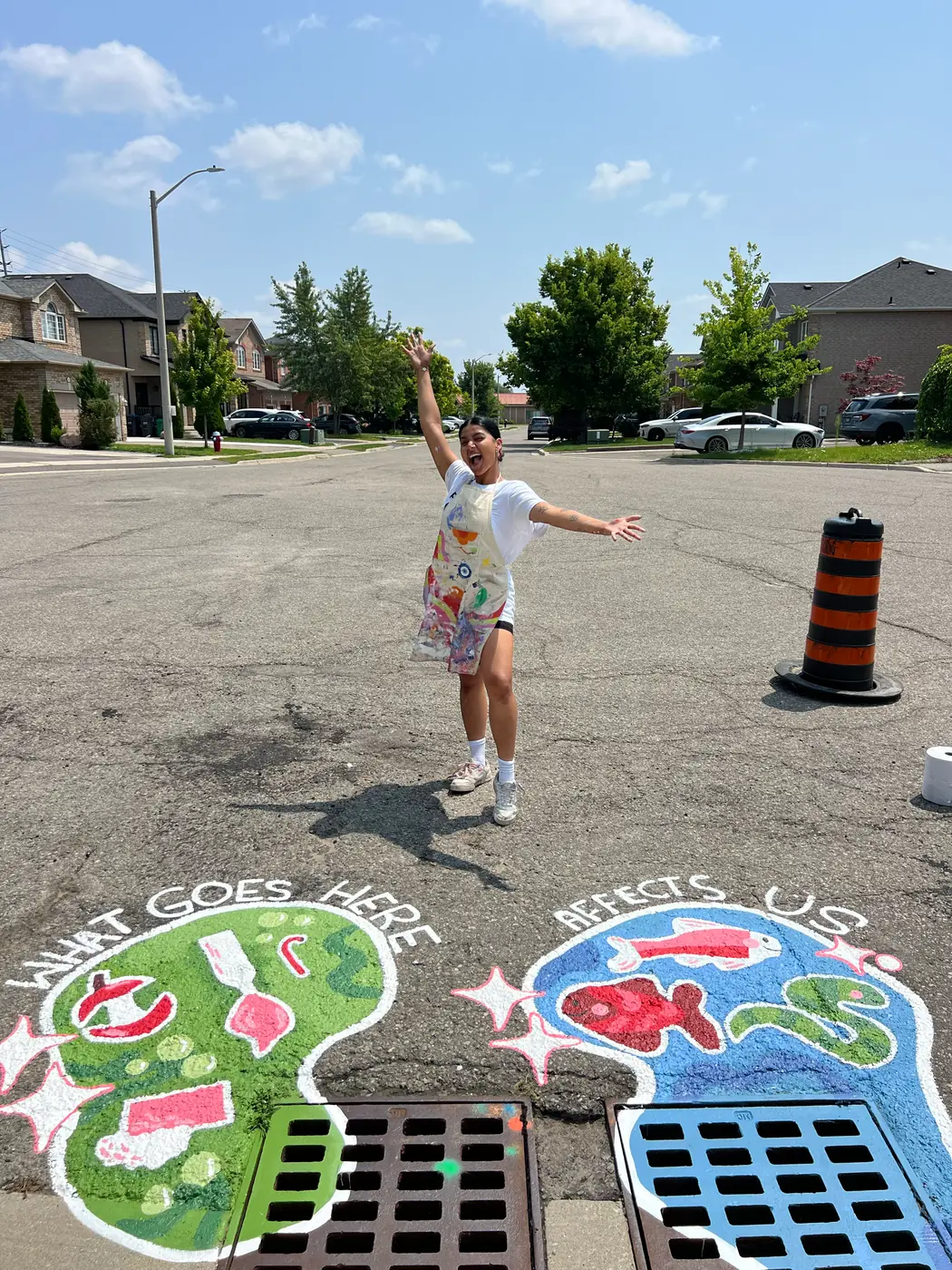 Saphera standing with arms outstretched on the street between the two finished catch basin murals