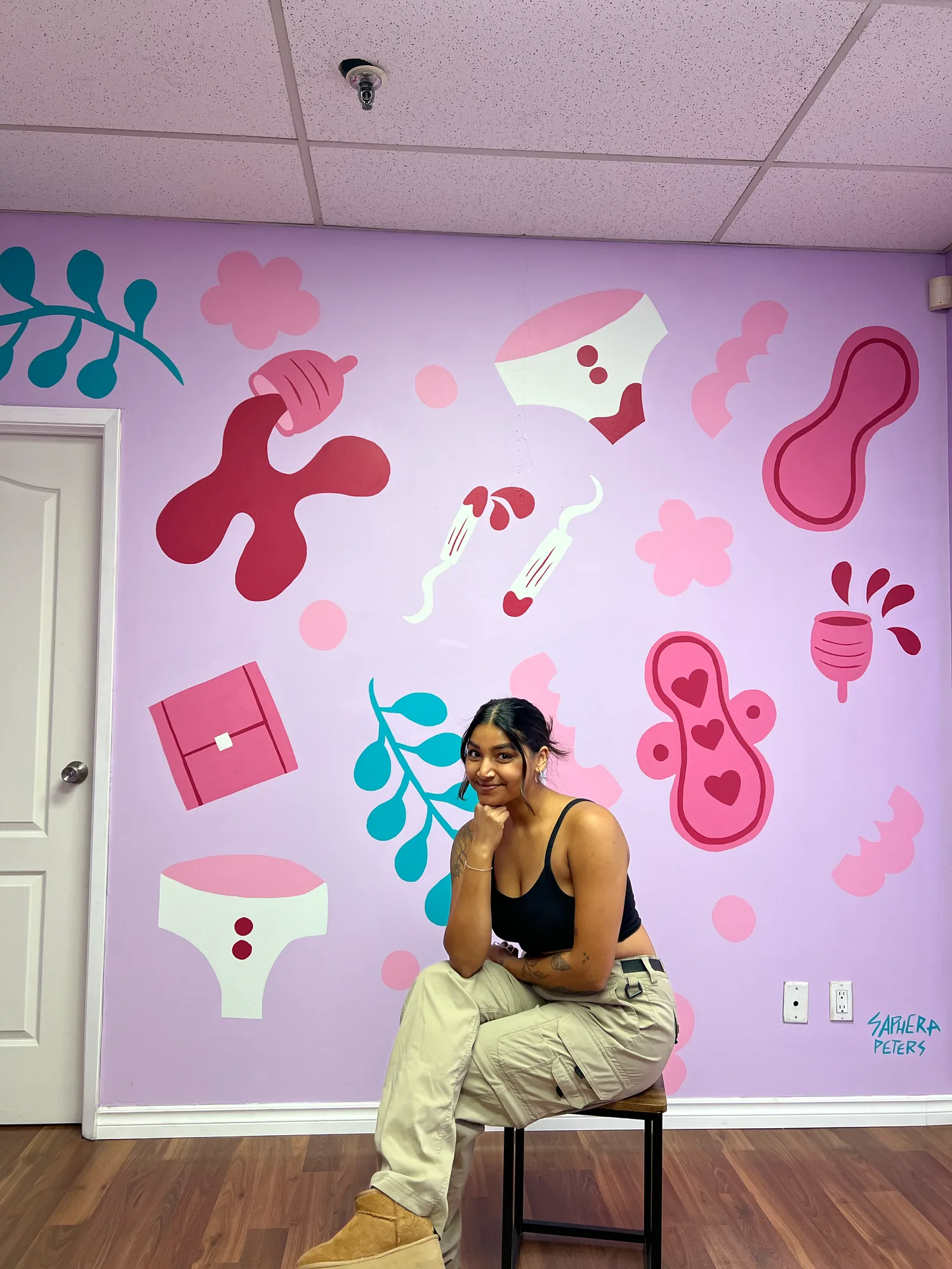 Saphera seated on a stool in front of the finished mural