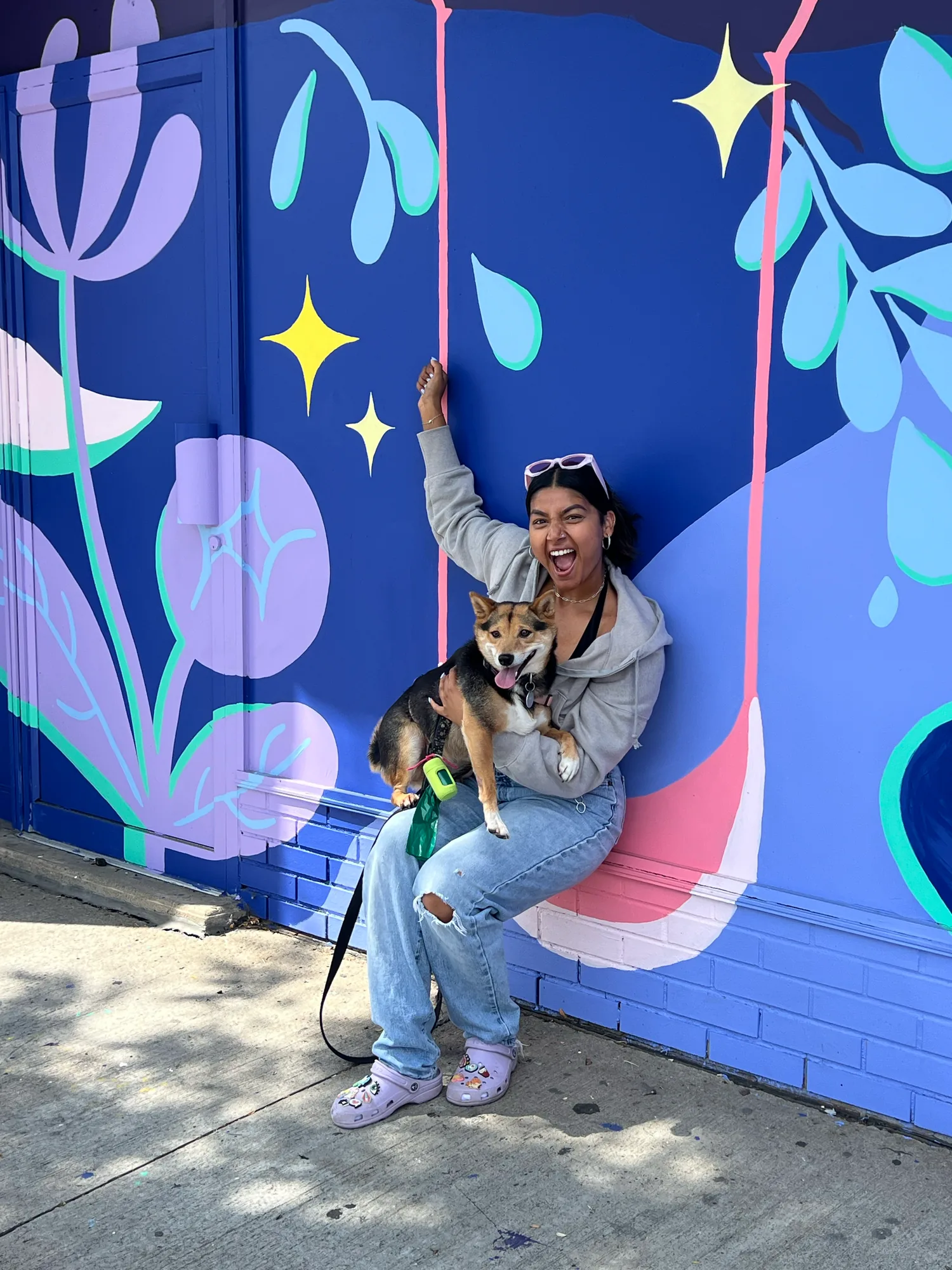 Saphera sitting in front of the finished blue and purple mural holding her dog