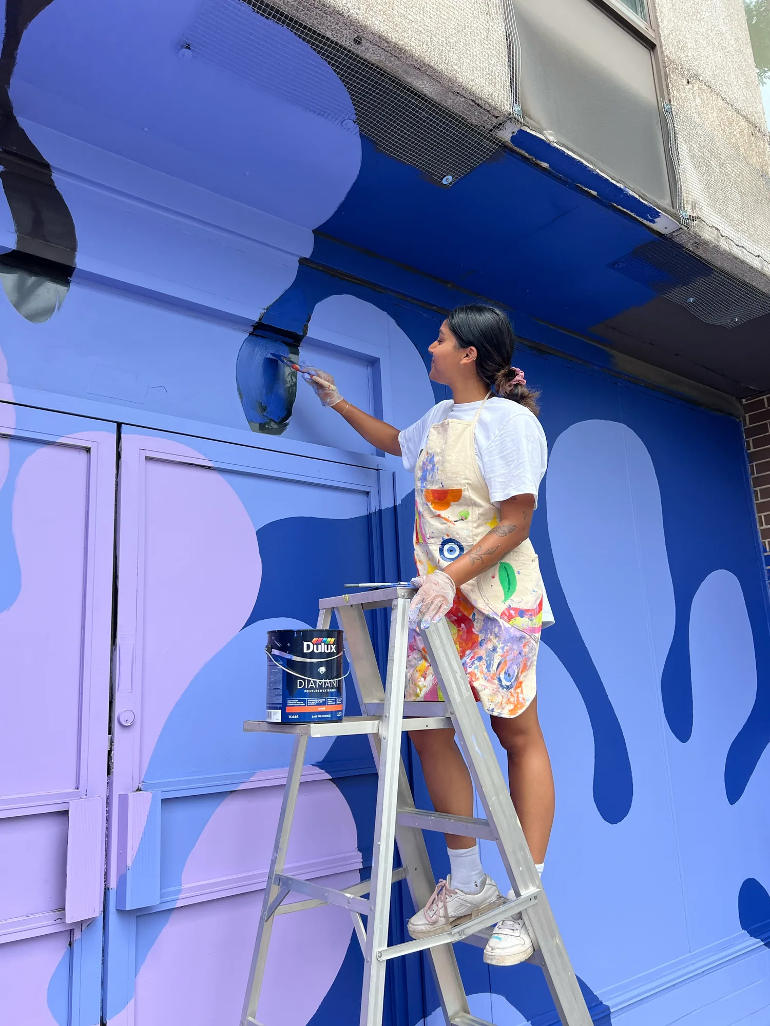 Saphera on a step ladder painting the purple section of the mural