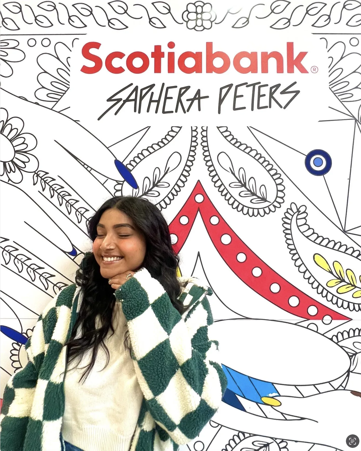 Saphera smiling beside the colouring wall with her name lettered alongside the Scotiabank logo