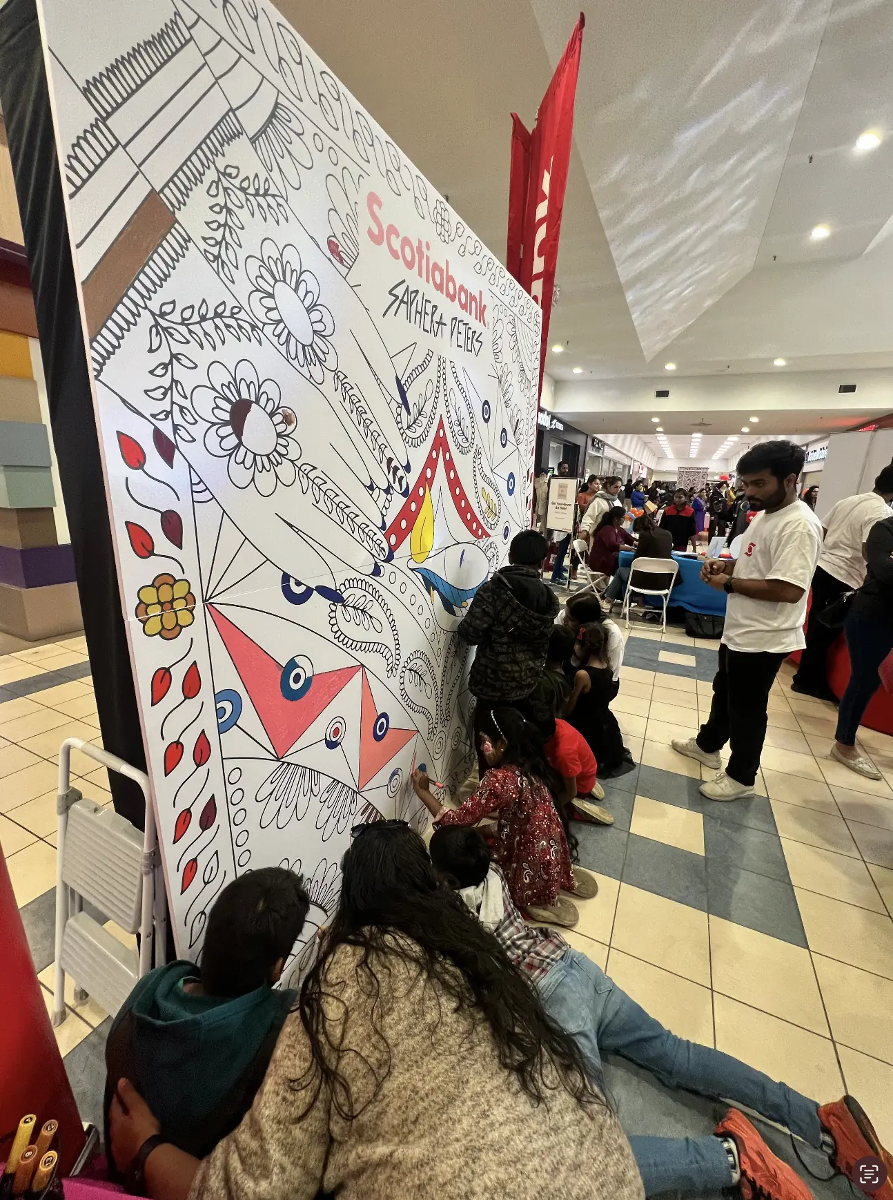 Event visitors kneeling at the base of the colouring wall filling in the illustration