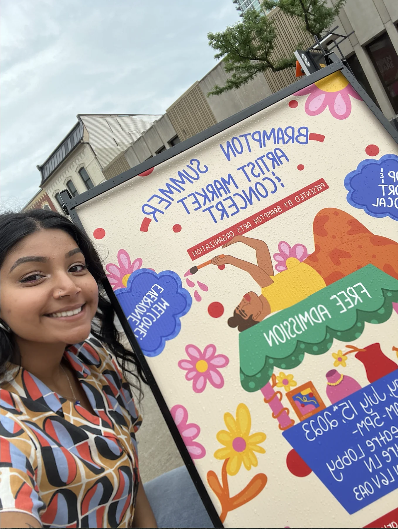 Saphera holding the large printed Summer Artist Market poster outdoors